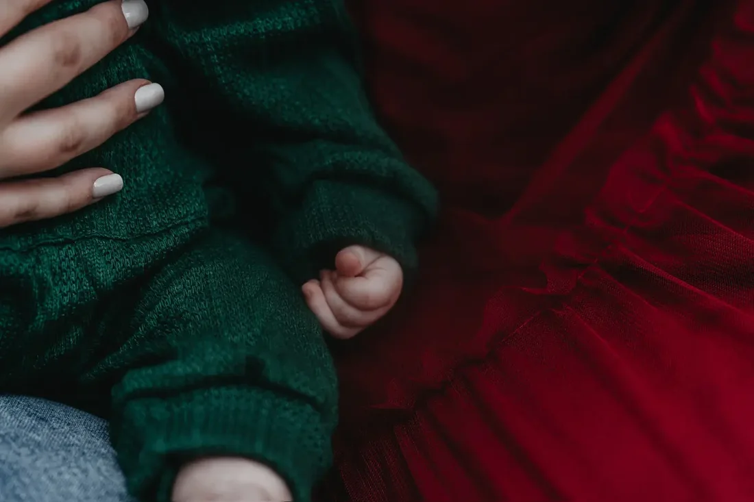 Baby's hand in a green sweater against a red dress, detail shot