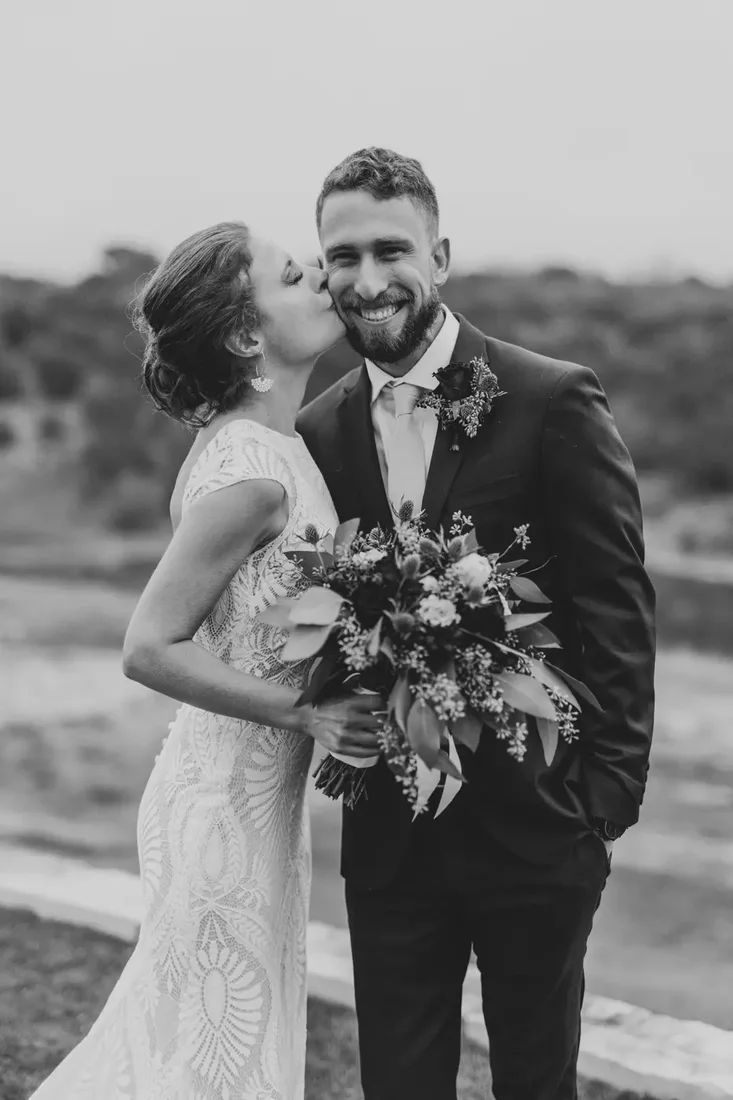Bride kissing her groom's cheek, black and white