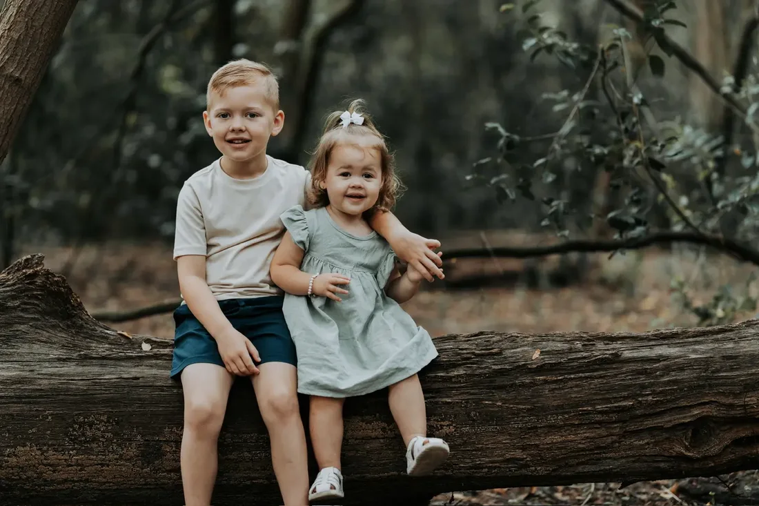 Brother and sister sitting on a log in the woods