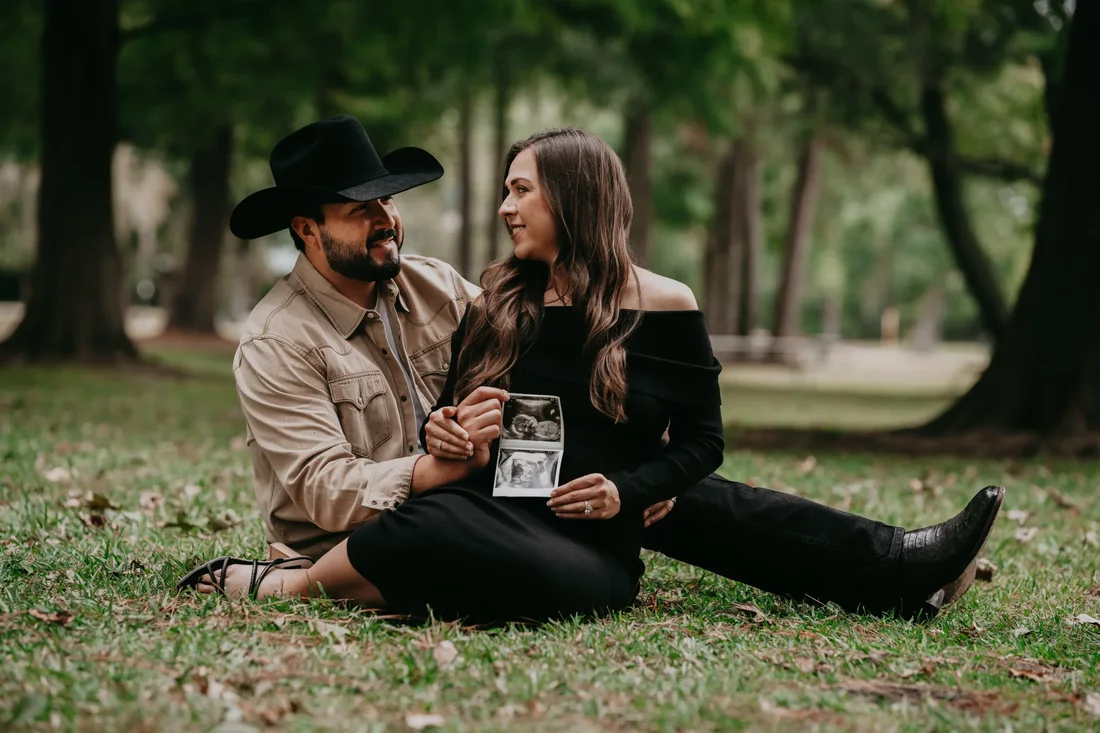 Couple sitting in the grass holding a sonogram photo