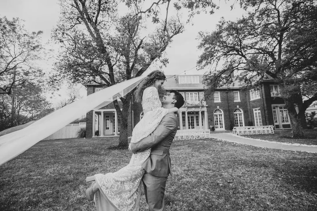 Groom lifting his bride outside the wedding venue, black and white