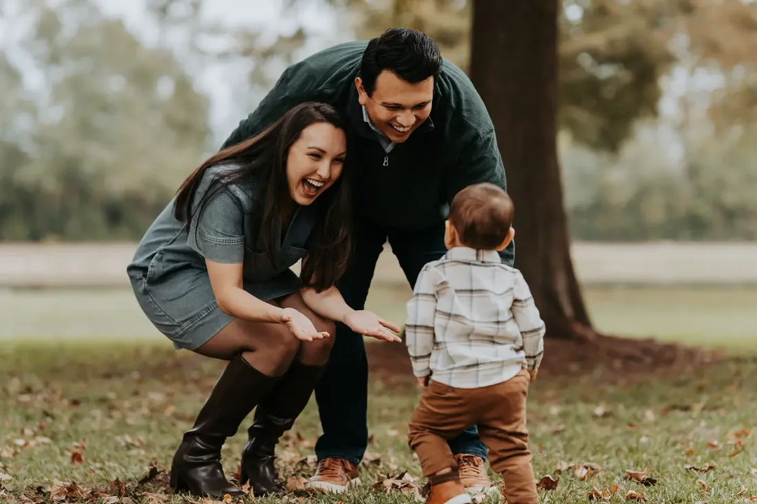 Parents crouching down to greet their toddler in fall leaves