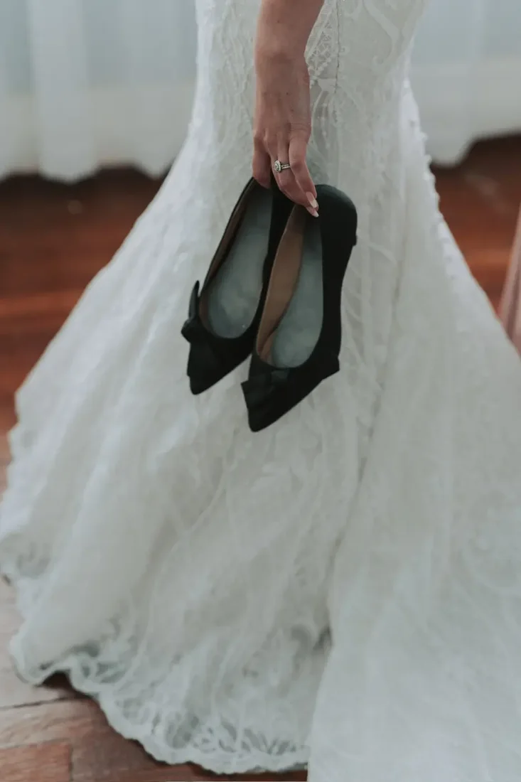 Bride holding her black bow shoes, wedding dress train